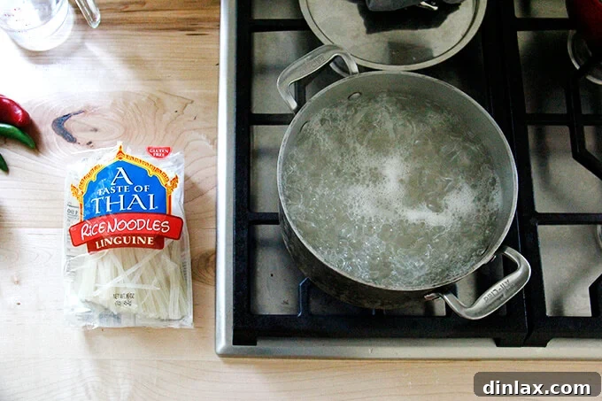 A stovetop with a pot of boiling water aside a package of rice noodles.