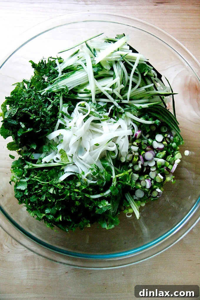 Cooked rice noodles with herbs and cucumbers in a bowl.