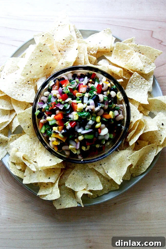 A bowl of fresh, colorful Texas Caviar, brimming with beans, corn, peppers, and herbs, served alongside crispy tortilla chips.