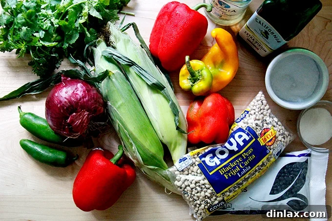 Assortment of fresh ingredients for Texas Caviar laid out on a kitchen counter, including bell peppers, red onion, corn, cilantro, jalapeño, and beans.