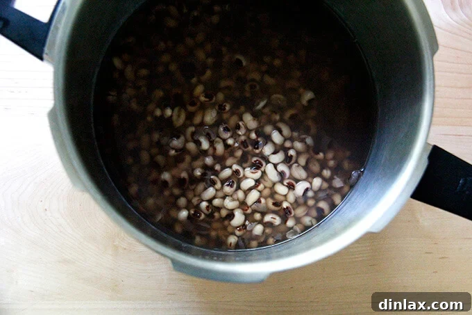 Cooked black eyed peas simmering in a stovetop pressure cooker, illustrating the bean cooking process.
