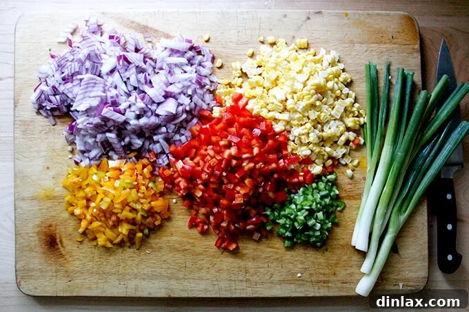 A cutting board filled with an array of precisely chopped vegetables and herbs for Texas Caviar, including bell peppers, red onion, corn, and cilantro.