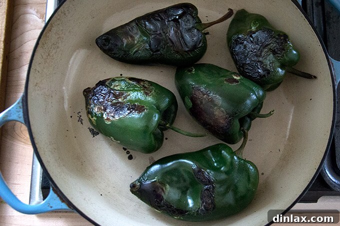 A close-up shot of perfectly blistered poblano peppers resting in a skillet after being charred, their skins softened and ready for peeling.