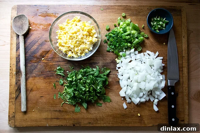 Freshly prepped ingredients including finely chopped onions, thinly sliced scallions, aromatic herbs like cilantro, a diced chili, and sweet corn kernels, ready for sautéing.