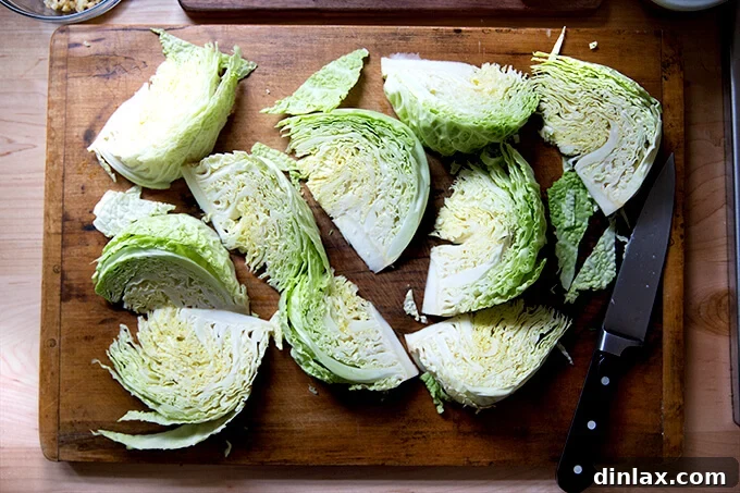 A wooden cutting board showcasing a head of Savoy cabbage expertly cut into neat, uniform wedges, ready for roasting.