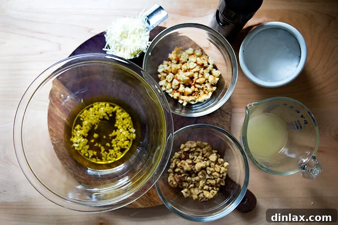 All the vibrant ingredients for the walnut salsa laid out: golden olive oil, finely minced garlic, shredded Parmesan cheese, crunchy bread crumbs, toasted walnuts, a fresh lemon half, and salt and pepper for seasoning.