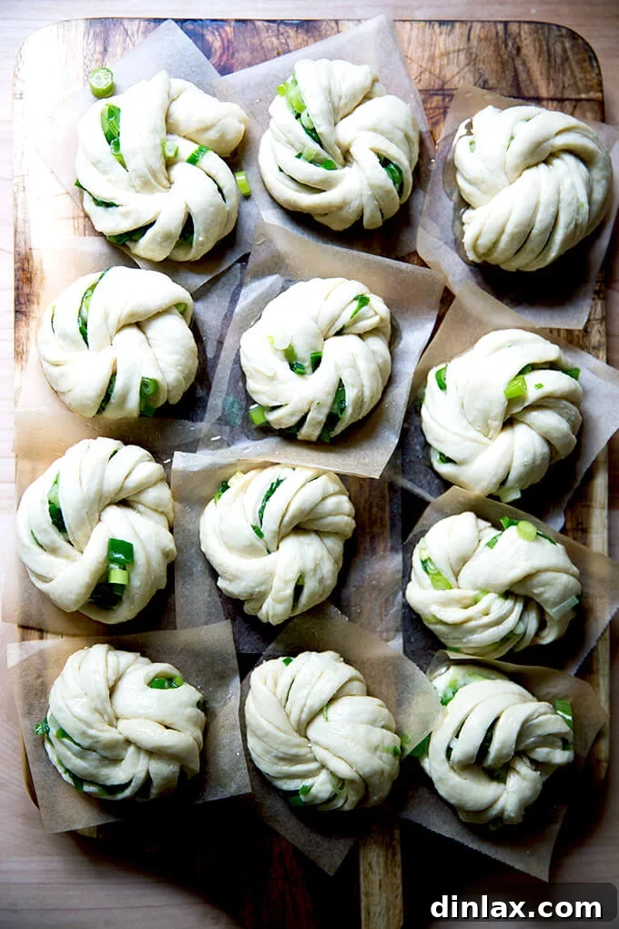 Chinese Steamed Scallion Twists 13 A close-up of a tray of unsteamed scallion buns, twisted into intricate knots, resting on parchment paper.