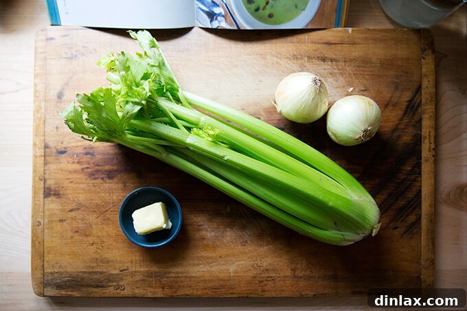 An overhead shot of fresh celery, onions, and butter laid out on a wooden cutting board, ready for soup preparation.
