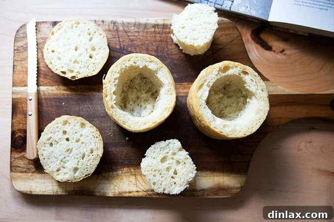 An overhead shot of two hollowed-out loaves of bread with their caps removed, perfectly prepared to become individual bread bowls for soup.