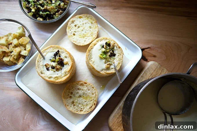 An overhead shot of two bread bowls filled with creamy celery soup, each topped with a generous spoon of vibrant walnut-currant salsa, presented beautifully on a wooden tray.