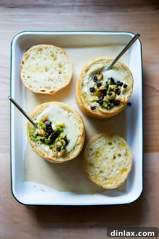 An overhead shot of two elegant bread bowls, each perfectly filled with smooth cream of celery soup and crowned with the colorful walnut-currant salsa.