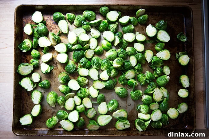 A sheet pan spread with perfectly arranged halved Brussels sprouts, olive oil, and salt, ready for the oven.