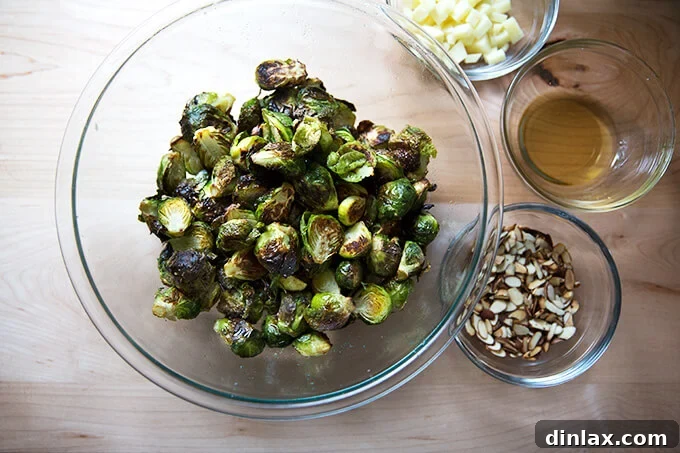 A bowl of freshly roasted Brussels sprouts, neatly arranged alongside separate bowls of Manchego cheese, toasted almonds, and rich reduced balsamic vinegar.