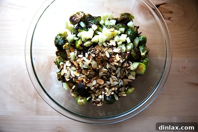 A bowl containing roasted Brussels sprouts, crunchy almonds, and savory Manchego cheese, ready for the final toss.