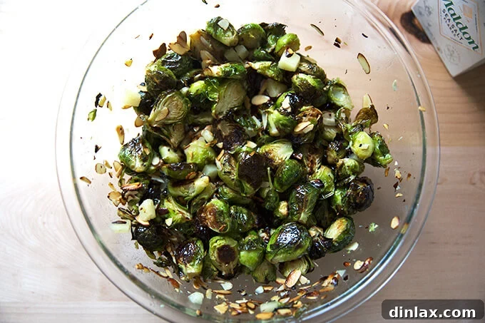 A bowl of roasted Brussels sprouts, almonds, and Manchego all thoroughly tossed together, glistening with balsamic, ready for tasting.