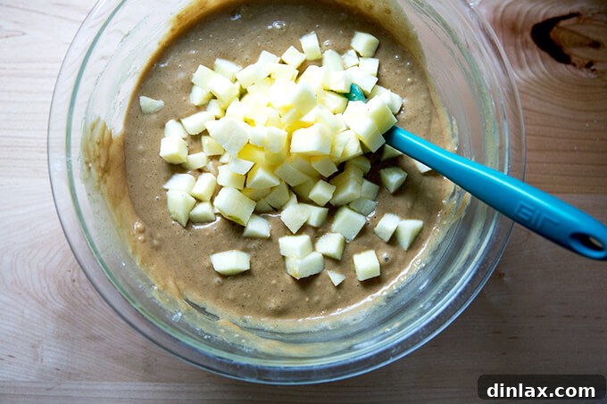 Harvest Apple Muffins 7 Finely chopped apples being folded into the muffin batter, ensuring even distribution throughout the mix.