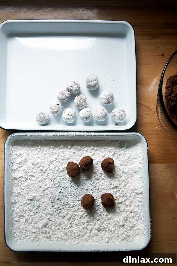 Quick and Boozy Holiday Rum Ball Delight 11 Two trays on a counter: one with finished, sugar-coated rum balls, and the other with the raw dough and powdered sugar for rolling.