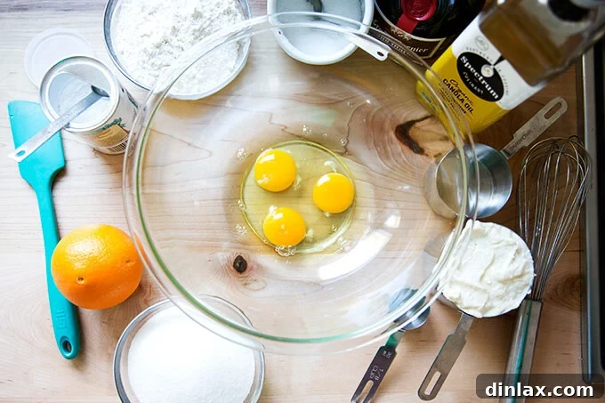 A selection of fresh ingredients laid out, including eggs, whole-milk ricotta, oil, orange liqueur, granulated sugar, salt, orange zest, baking powder, and all-purpose flour, ready for baking the orange ricotta pound cake.