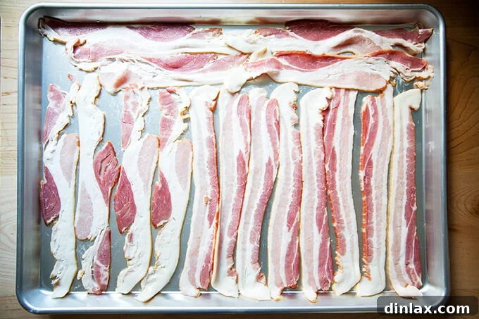 Bacon strips arranged on a parchment-lined sheet pan, ready for the oven