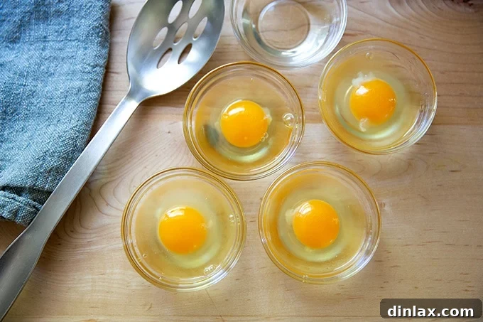 Four eggs cracked into individual small bowls, ready for poaching.