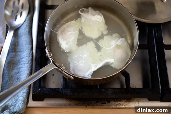 A shallow pot holding water and 4 poached eggs, covered with a lid to cook.