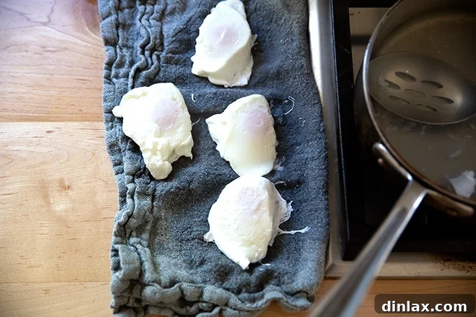 Four perfectly poached eggs resting on a napkin, ready to be served.