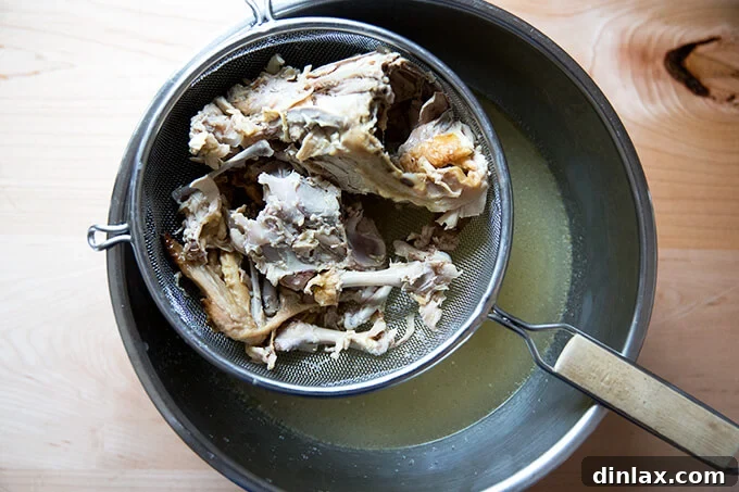 Homemade chicken stock being strained through a fine-mesh sieve into a large bowl.
