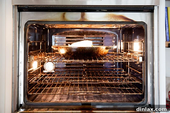 A whole chicken roasting in a skillet inside a hot oven.