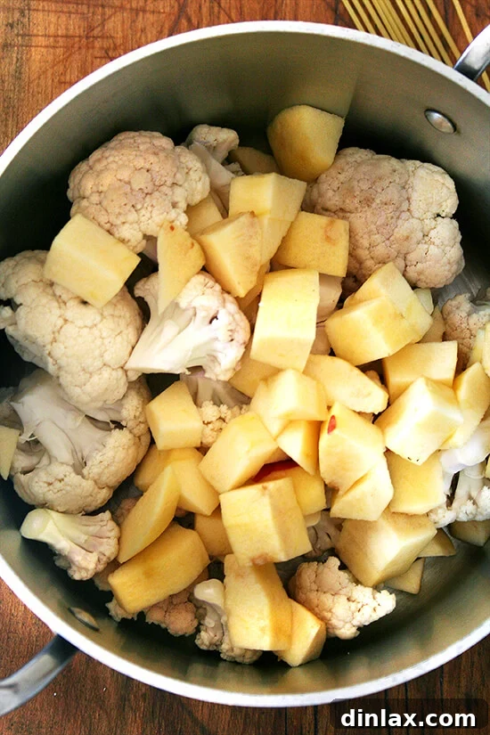 Cauliflower florets and chopped apples simmering in milk in a large pot