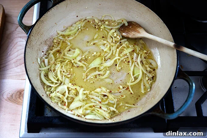 Minced garlic and crushed red pepper flakes being added to the sautéed onions in the pan.