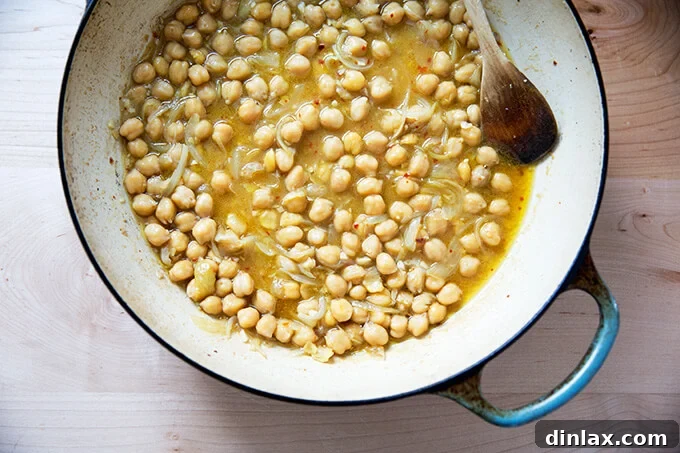 Brothy, stewy, and spicy chickpeas simmering in a pan, infused with garlic and red pepper flakes.