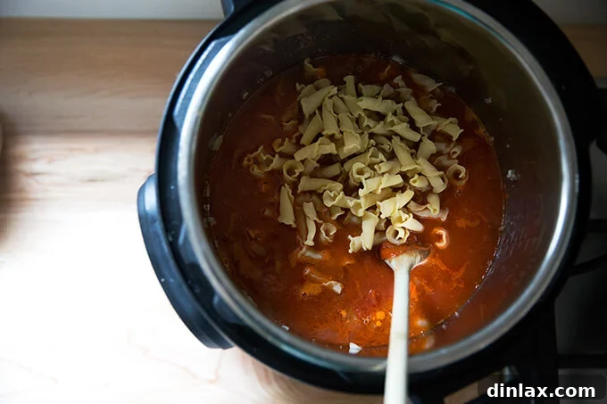 Effortless Instant Pot One Pot Pasta and Meat Sauce 6 Uncooked pasta, marinara sauce, and water being added to the browned meat mixture in the Instant Pot.