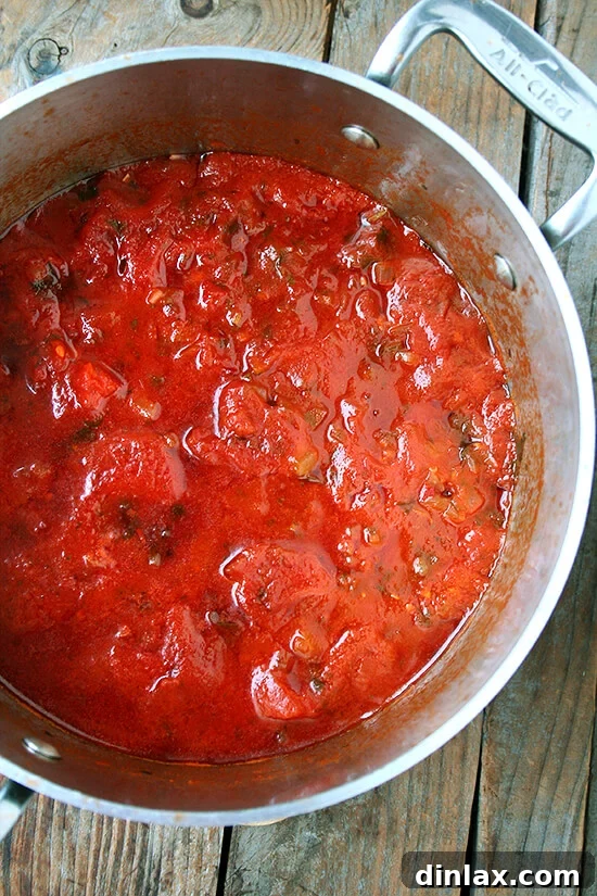 The Marcella Hazan tomato sauce simmering gently, with onions, garlic, white wine, parsley, and red pepper flakes creating a vibrant aroma.