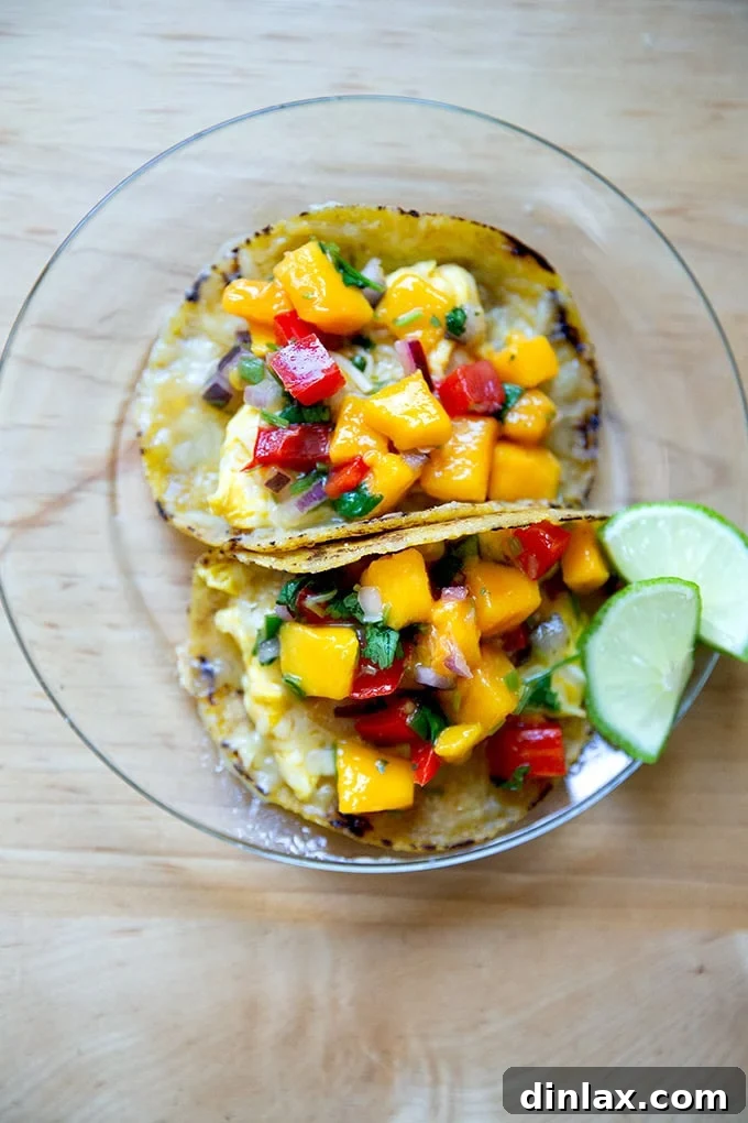 Two enticing breakfast tacos, crafted with homemade corn tortillas, generously filled with scrambled eggs and topped with a vibrant homemade mango salsa, ready to be devoured.