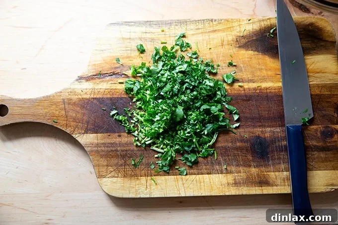 Freshly chopped cilantro, including stems and leaves, gathered neatly on a cutting board, ready to be incorporated into the vibrant salsa mixture.