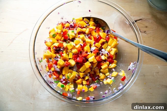 A large bowl of mango salsa, perfectly seasoned with salt and lime juice, undergoing its initial toss to combine flavors before cilantro is added.
