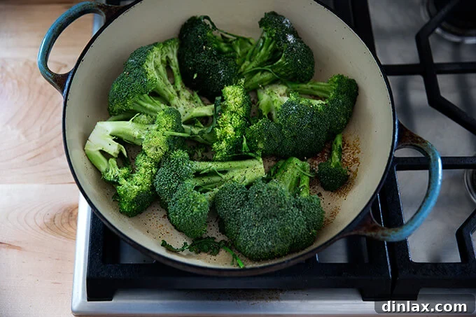 Broccoli searing in a hot skillet, cut-side down, developing a beautiful char.
