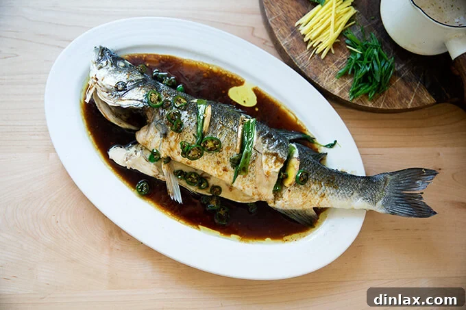 Ginger-Scallion Infused Steamed Whole Fish 15 Steamed Branzino on a platter, glistening with hot oil and savory soy sauce.