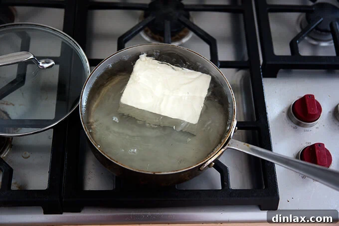 Velvety Tofu with a Garlic Kick 5 A whole block of firm tofu simmering gently in water within a saucepan.