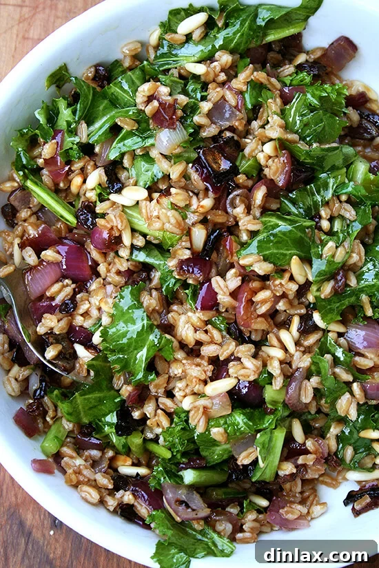 A beautifully presented bowl of farro salad, brimming with roasted onions, glistening toasted pine nuts, and tender wilted mustard greens, ready to be enjoyed.