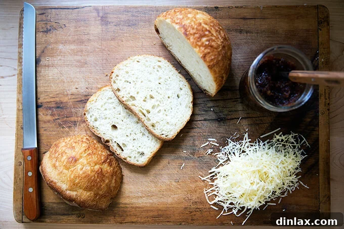 Versatile Apple Chutney Brightened with Ginger and Lemon 9 A rustic wooden board featuring slices of artisan peasant bread, a jar of homemade apple chutney, and a mound of grated cheese, illustrating serving suggestions.