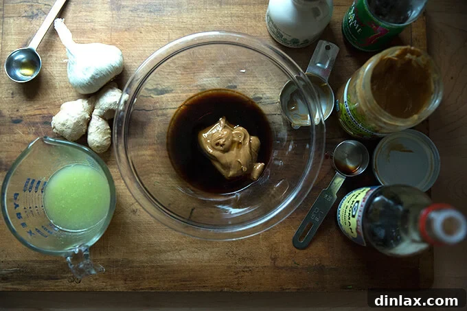 A close-up of a whisk stirring together the creamy peanut-ginger dressing ingredients in a bowl.