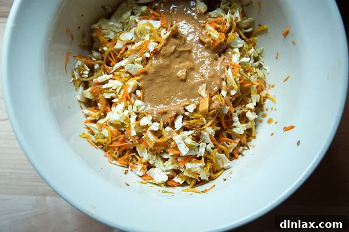 The vibrant peanut dressing being poured over the bowl of shredded cabbage, carrots, and beets, ready for tossing.