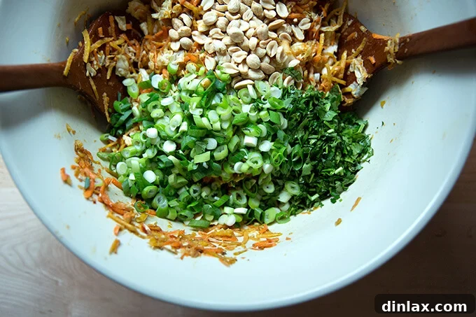 Chopped scallions, fresh cilantro, and toasted peanuts being added to the bowl of dressed cabbage and other vegetables.