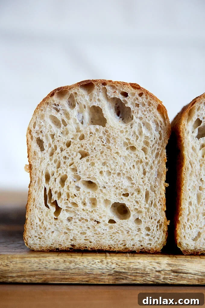 A rustic cutting board holding a tall, square-shaped sourdough toasting bread loaf.