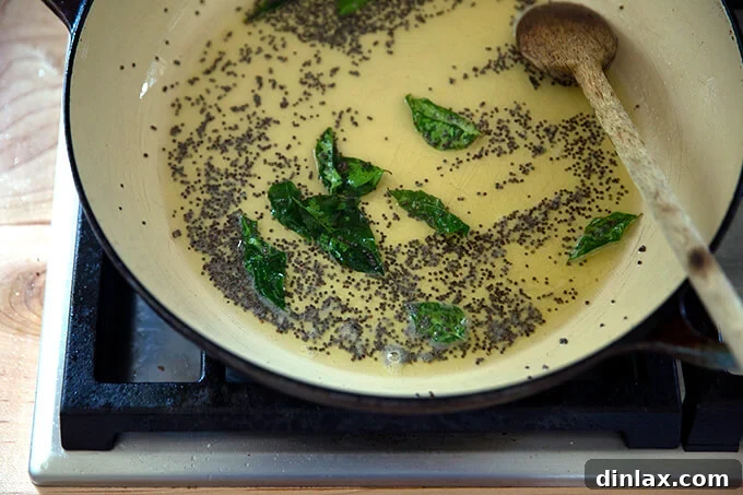 Fragrant curry leaves added to the shimmering ghee and popping mustard seeds in a braiser pan, intensifying the aromatic base.