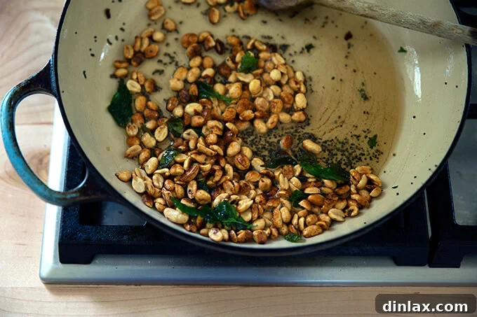 Roasted peanuts joining the ghee, mustard seeds, and curry leaves in the braiser pan, preparing to be lightly toasted and infused.
