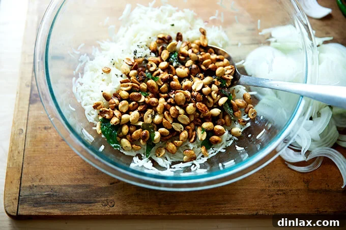 The spiced ghee, mustard seeds, curry leaves, and peanuts mixture being poured over the prepared basmati rice in a large bowl, ready for tossing.