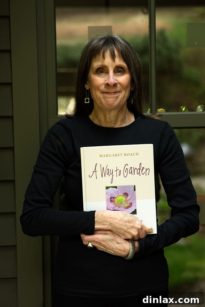 Margaret Roach smiling brightly, holding her newly released book, A Way to Garden, in her lush garden.