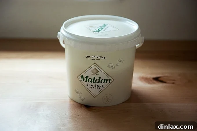 A large, distinctive bucket of Maldon Sea Salt flakes, a gourmet kitchen essential.